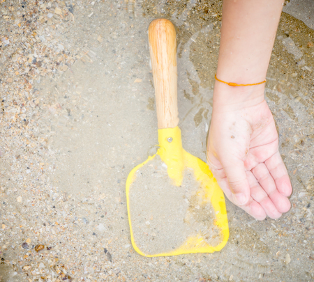 Kid hand and Toy shovel on Sand Sea water surfaceの写真素材