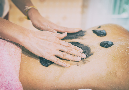 Spa therapist is rubbing charcoal coffee scrub on women back skinの写真素材