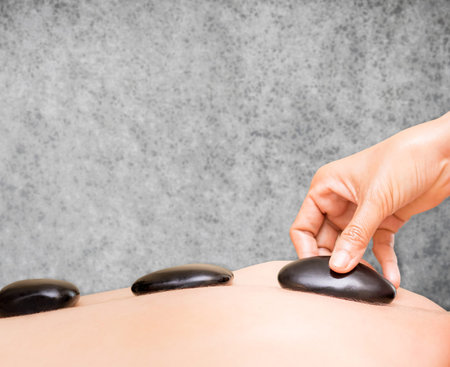 Hand is placing black hot stone on a women back with concrete copy space