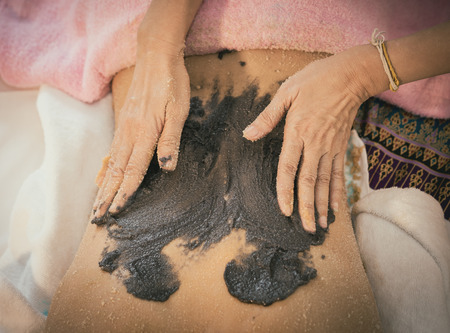 Spa Therapist is applying Charcoal coffee scrub on to a woman backの写真素材