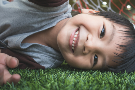 Little kid smiling while lying down on soccer fieldの写真素材