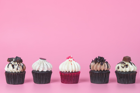 Five chocolate cupcake with red cupcake in the middle on pink backgroundの写真素材