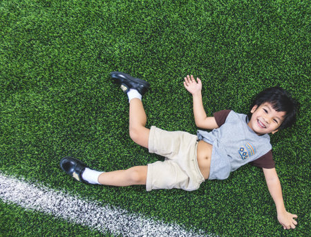 Little boy is lying down on soccer field top view