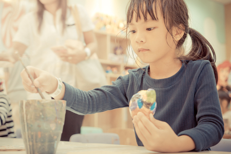 Little girl is painting a doll in art classroomの写真素材