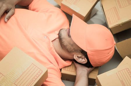 Delivery guy in orange sleeping on packaging boxesの写真素材