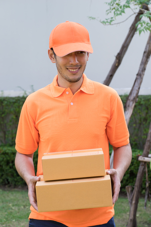 Delivery man in orange bringing package to your homeの写真素材