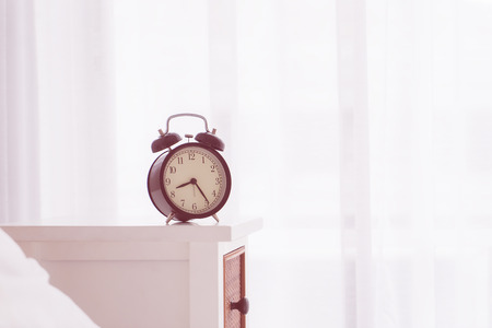 Vintage alarm clock on bedside table by morning windowsの写真素材