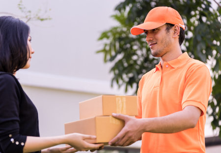 Delivery man in orange is handing packages to a womanの写真素材