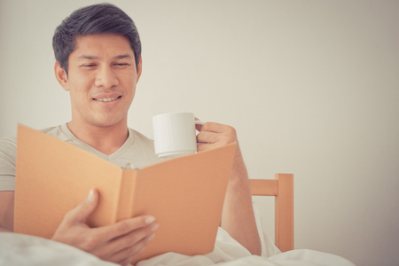 Asian male is studying and drink coffee on morning bedの写真素材