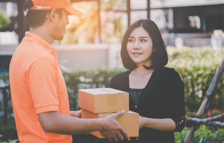 Delivery man in orange is handing packages to a womanの写真素材