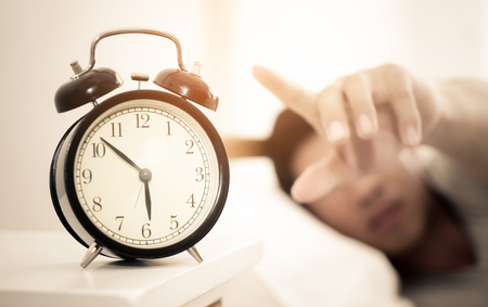 Man hand reaching out to alarm clock for snoozeの写真素材