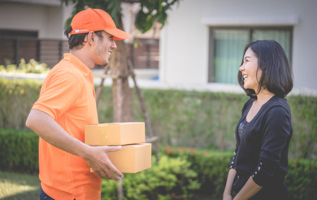 Delivery man in orange is handing packages to a womanの写真素材
