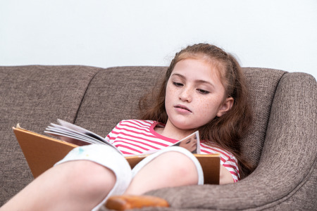 Happy Little girl is reading book on sofaの写真素材