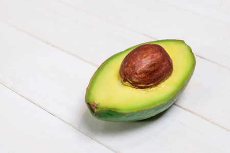 One half of avocado on white wooden backgroundの写真素材