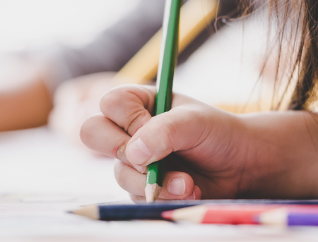 Child hand is using color pencil to practice writing on a paper.の写真素材