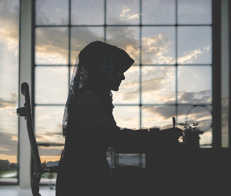 Muslim woman is working on office tabl e silhouette with sunset skyの写真素材