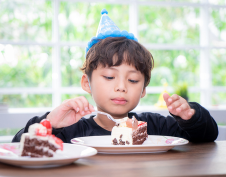 Kid with party hat is eating birthday cakeの写真素材