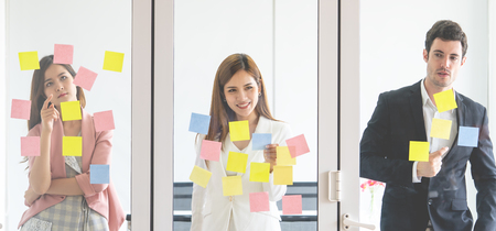 Three Business people is writing idea on to sticky notes windows for team planの写真素材