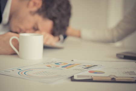 Tired business man fall asleep on office tableの写真素材