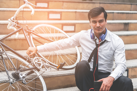 Business man is relaxing listening to music with his bicycle on the sideの写真素材