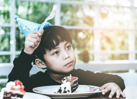Asian Kid with party hat is eating birthday chocolate cakeの写真素材