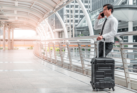 young business man man on business trip standing with his luggage and making a call outside airport. Business traveler making phone callの写真素材