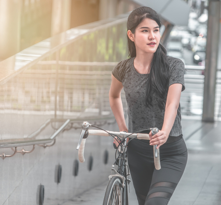 Asian girl on bike in the city in the morning with sun flareの写真素材