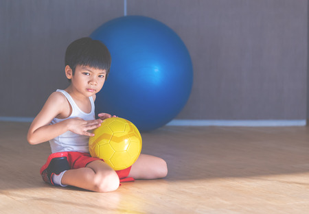 Young boy is sitting with soccer on the floorの写真素材