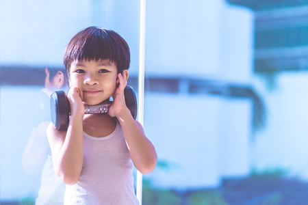 Little boy is working out with dumbbell by the windows city.の写真素材