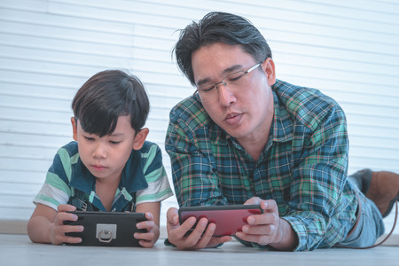 Asian Father is teaching his son to use the smartphone and internet on the floorの写真素材