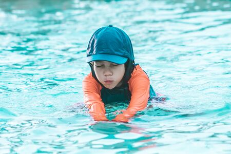 Little Girl in orange and blue suit is swimming in a water park poolの写真素材