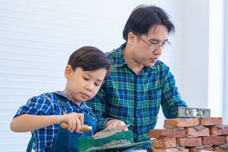 Little boy is learning how to lay down brick work from his builder fatherの写真素材