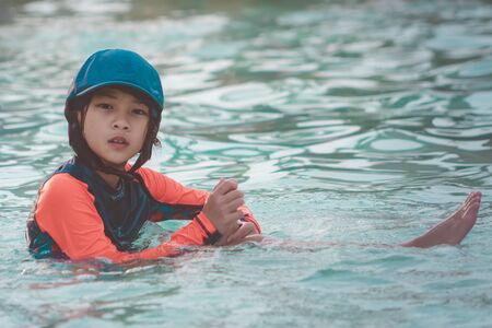 Tired Asian kid girl is sitting in kid swimming poolの写真素材
