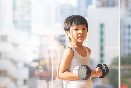 Little boy is working out with dumbbell by the windows city.の写真素材