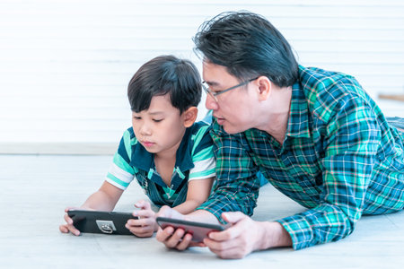 Asian Father is teaching his son to use the smartphone and internet on the floor