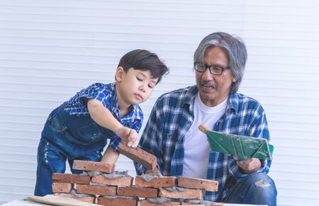 Little boy is learning how to build brick wall from his construction grandfatherの写真素材
