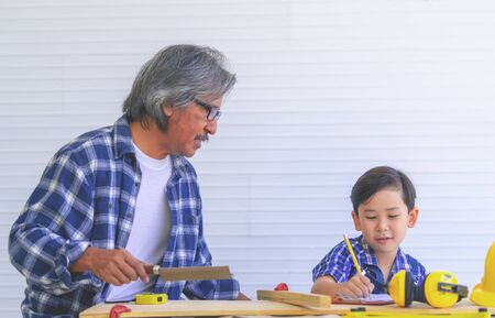 Builder Grandfather is teaching his boy to work on construction woodwork tools.の写真素材
