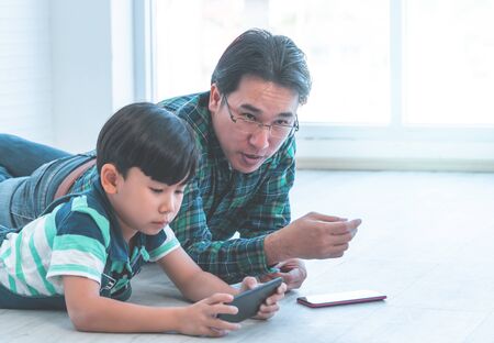 Asian Father is teaching his son to use the smartphone and internet on the floorの写真素材