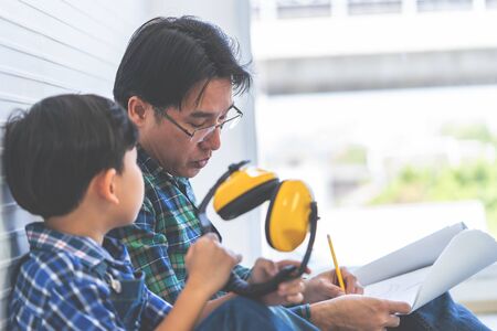 Builder Father is teaching his son to read the construction plan paper.の写真素材