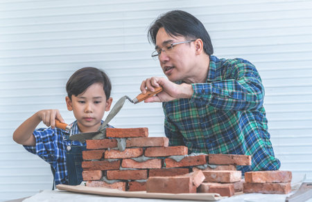Little boy is learning how to lay down brick work from his builder fatherの写真素材