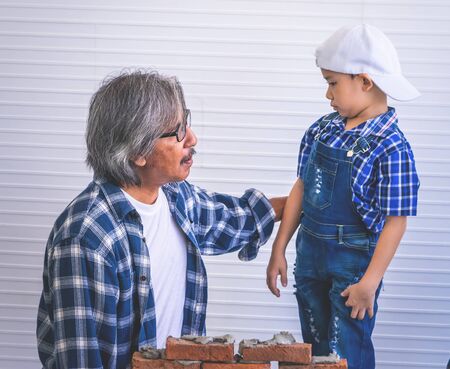 Little boy is learning how to build brick wall from his construction grandfatherの写真素材