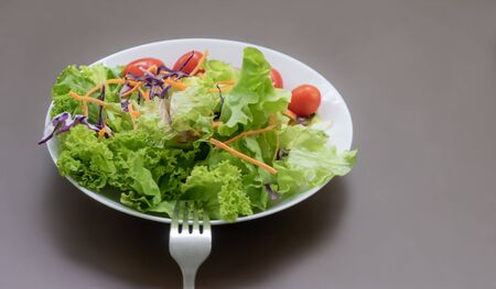 Green fresh vegetable salad on white place and brown tableの写真素材