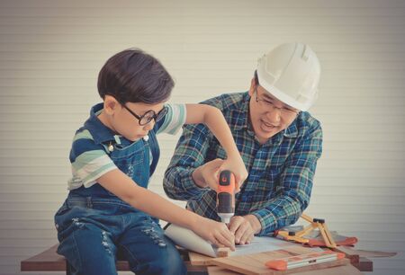 Little Boy is learning to work on wood and be a builder from his craftman father in vintage toneの写真素材