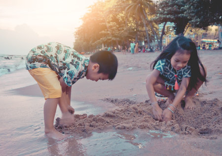 Two siblings Asian children is playing with wave and sand in Pattaya Beach Thailand for family and kid summer holidays conceptの写真素材