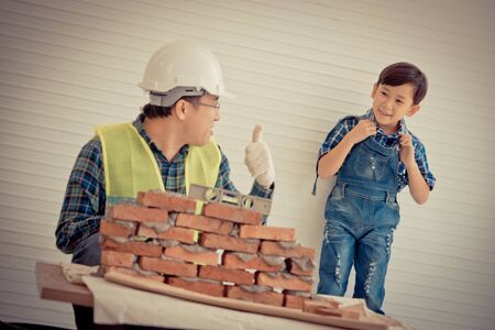 Little Boy is learning to work on Brickwall and be a builder from his craftman father in vintage tone, Family working together on house renovation for family bonding togetherness.の写真素材