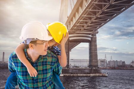 Father builder is carrying his son  in modern city Bridge Sunset for industry and family boding future conceptの写真素材