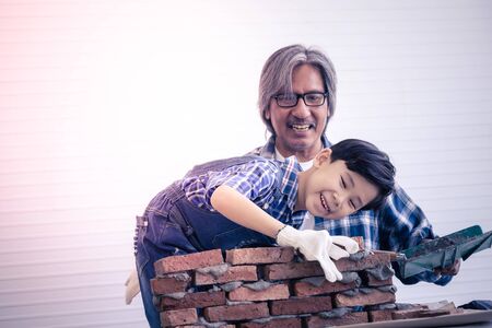 Little boy is learning how to lay down brick work from his builder father in vintage toneの写真素材