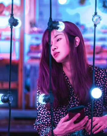 Portrait of a woman on bright Bokeh light on chair decoration in Outdoor Festive Market in Neon color tonedの写真素材