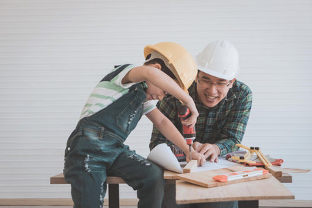 Father and son is drilling wood on workshop table for home improvement, for family bonding father...