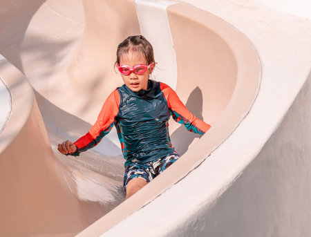 Little girl is sliding down the water slide in aqua park children playground.
